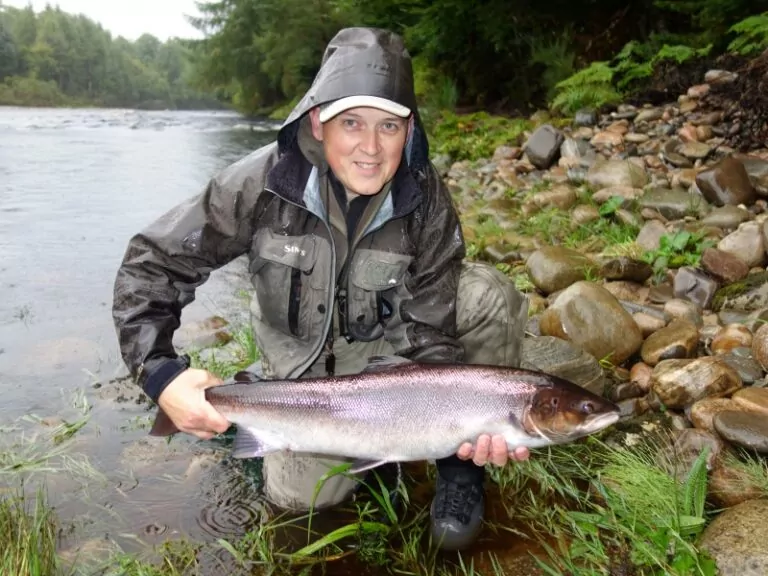 A man in a raincoat holding up a fish.