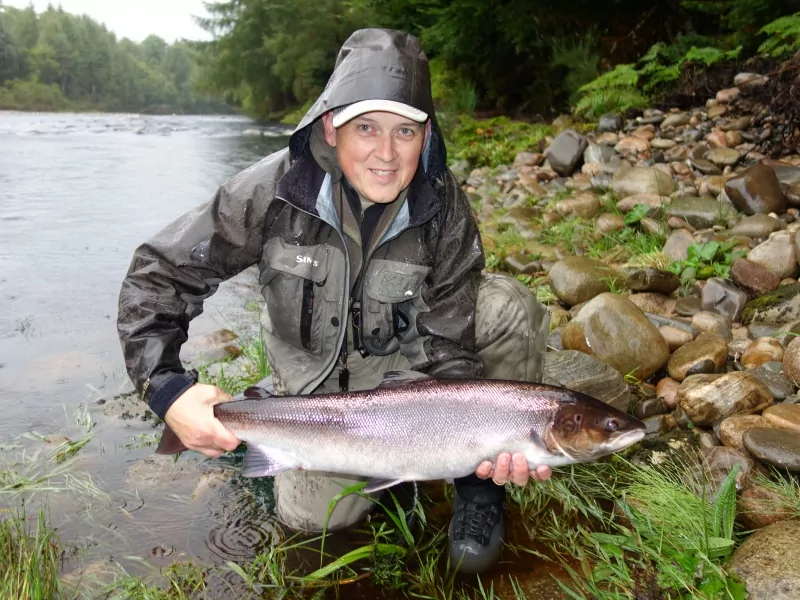 A man in a raincoat holding up a fish.