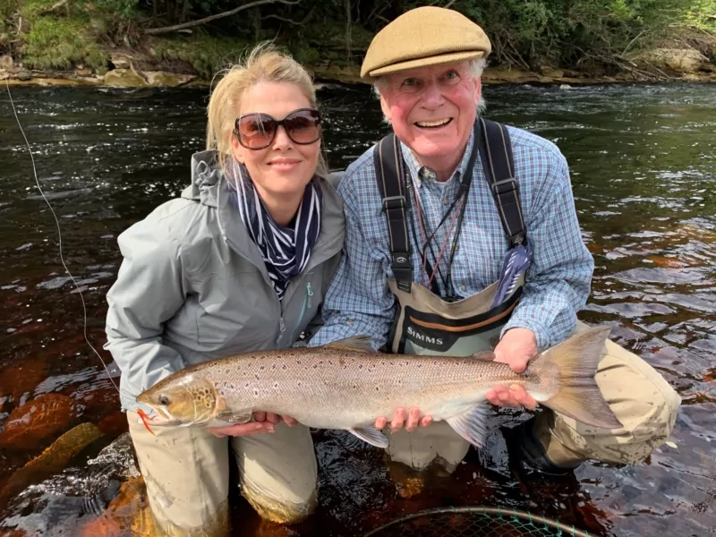 A man and woman posing with a fish in a river.