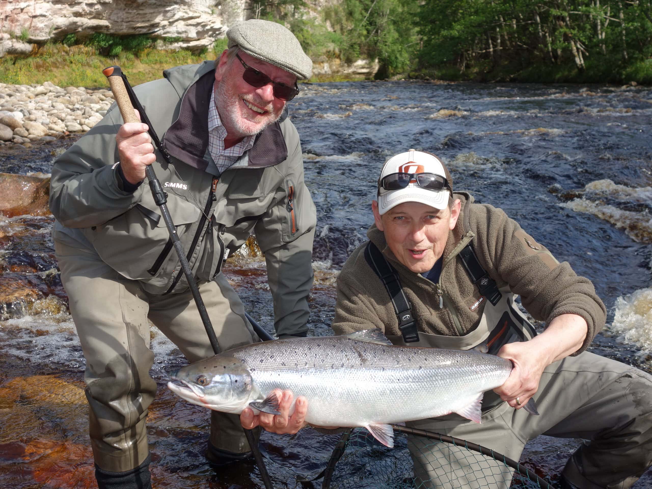 Two men holding up a fish in a river.