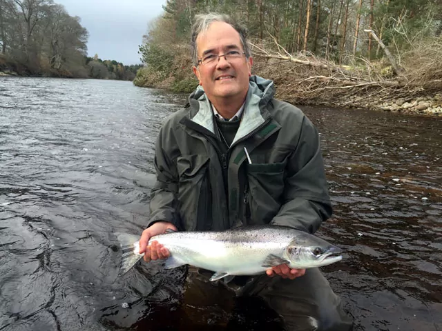 A Speycaster holding up a fish in a river.