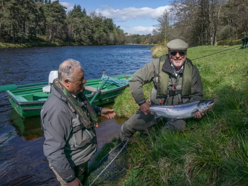 Two men standing next to a boat holding a fish.