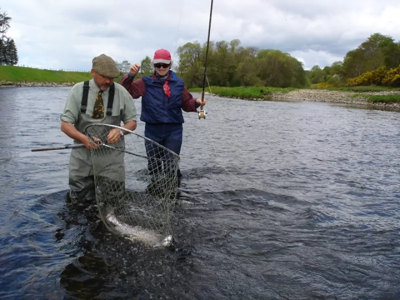 Two people fishing in a river with a net.