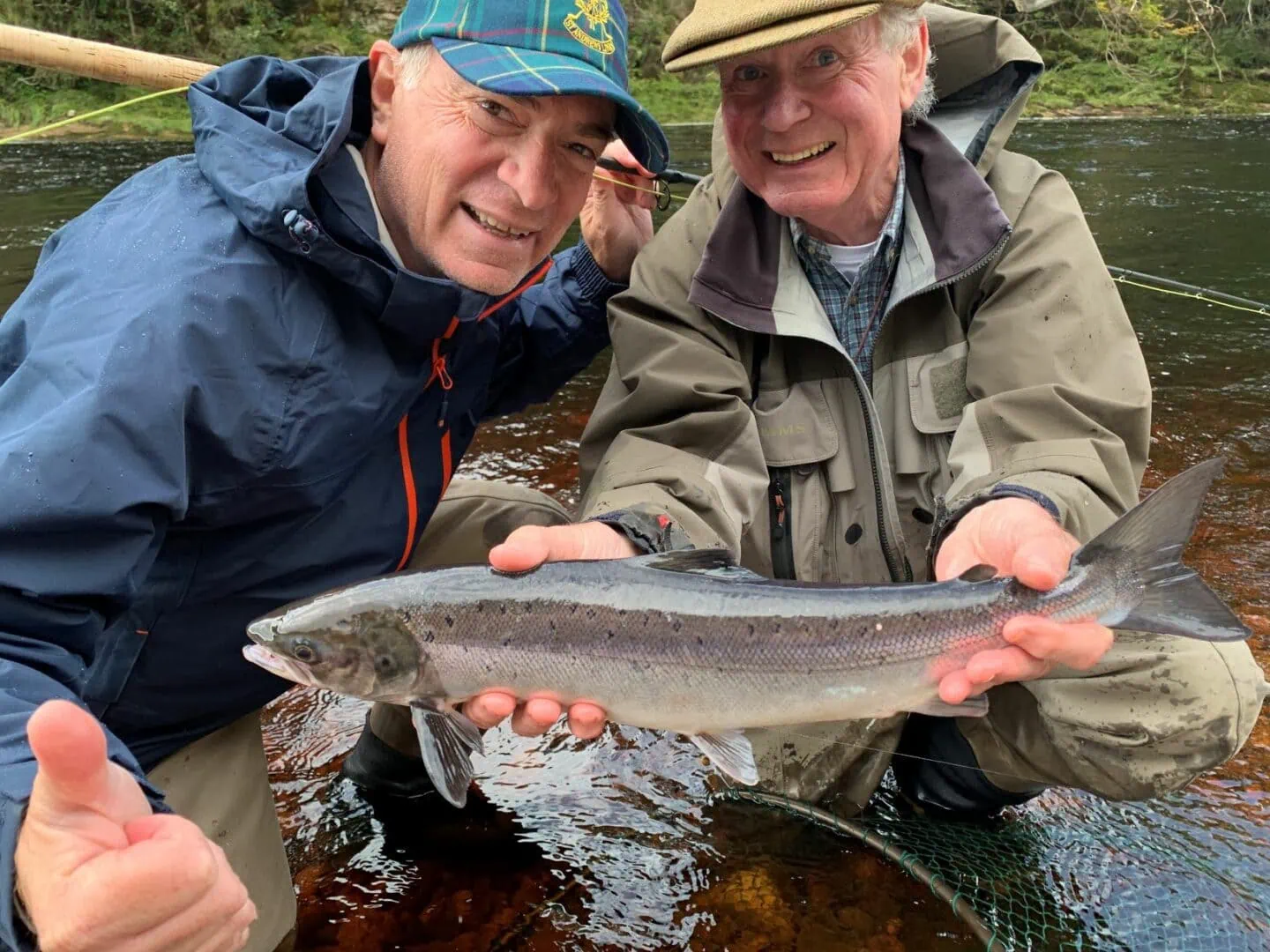 Two men holding up a fish in a river.