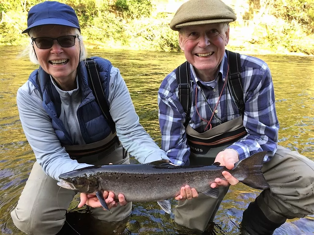 Two people holding up a fish in a river.