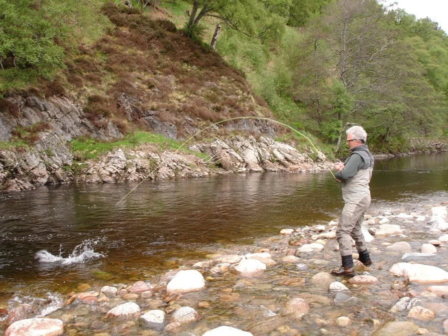A man is standing on a river with a fly rod in his hand.