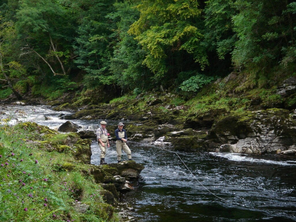 Two people standing on the side of a river.