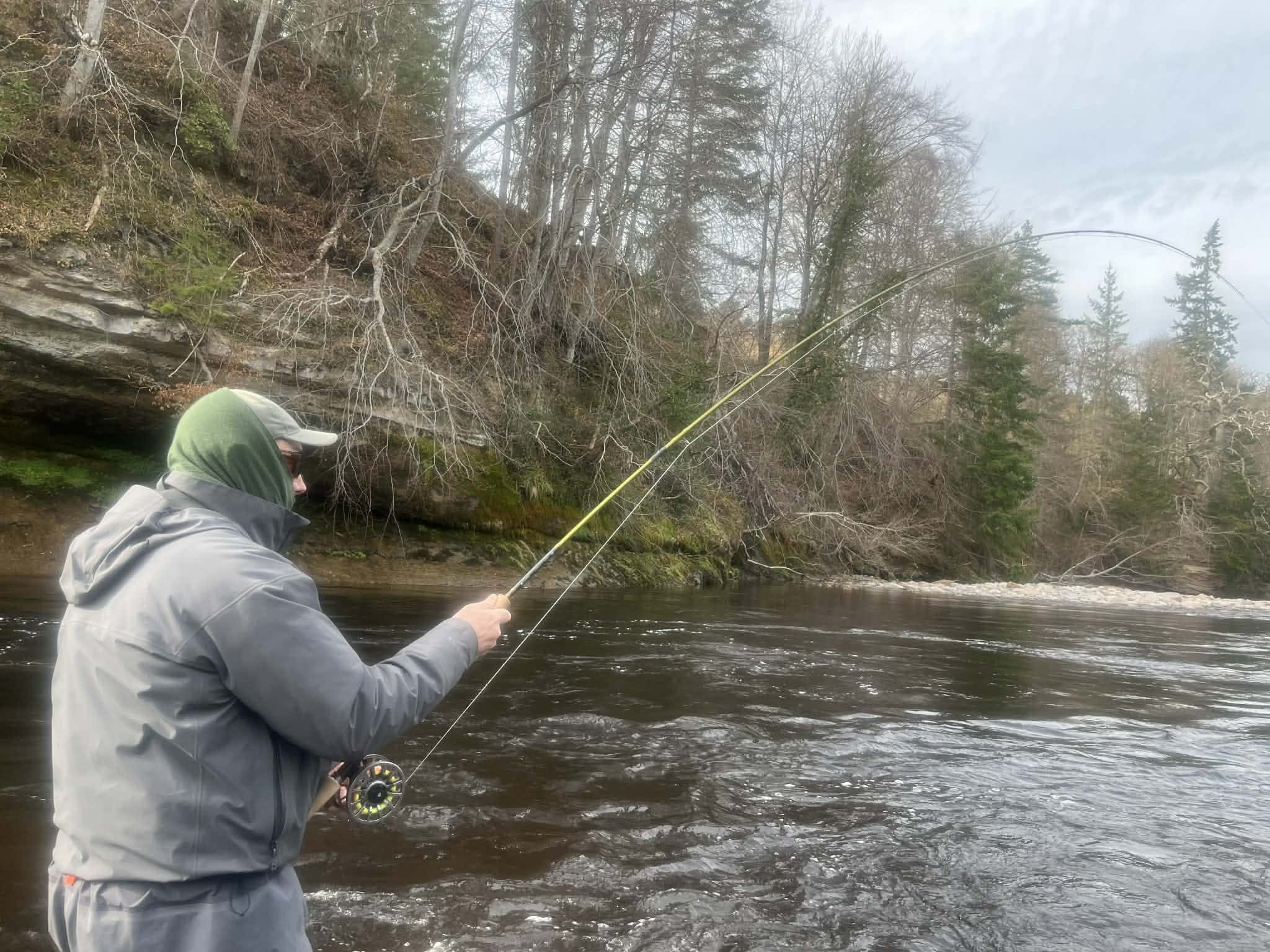 Angler casting a fly rod on the River Findhorn in spring 2026 with rocky cliffs and trees in the background